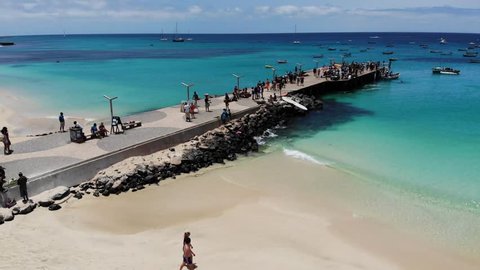 Aerial footage of the famous pier at Cape Verde, fishermen with fishermen's wives selling the fish on the pier, taken in Santa Maria beach in Sal Cape Verde Cabo Verde taken with a drone on sunny day