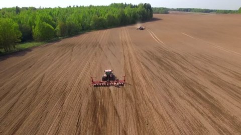 Two Row Crop Tractors going in the opposite direction and cultivating land. Aerial of red tractor on harvest field (top view from height).