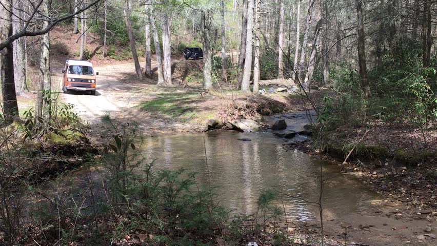An orange campervan crossing a river.