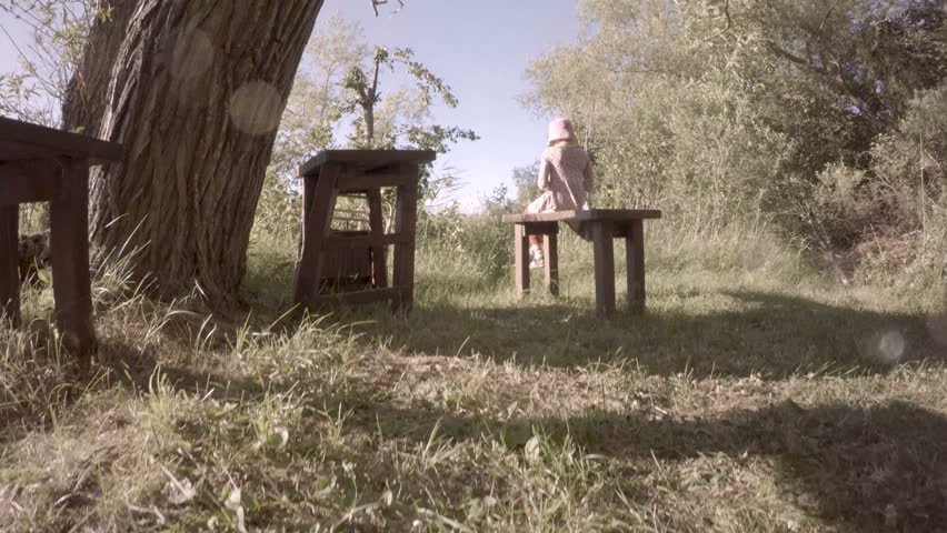 Little girl sitting on wooden bench. Calm and beautiful nature scene. Peaceful and idyllic summer landscape.