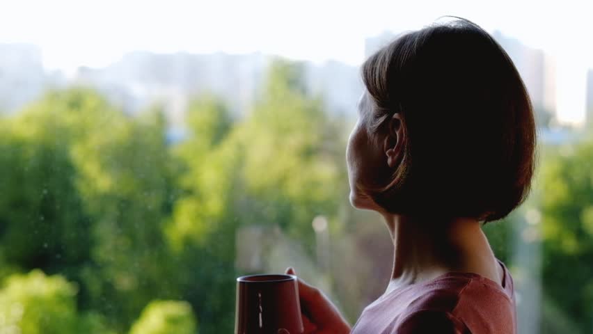 Woman standing at the window and drinking coffee or tea | Shutterstock HD Video #1011371837