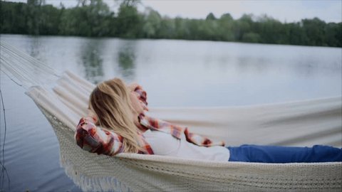 Young woman by the lake hanging on hammock relaxing in the morning. People relaxation travel concept. SLOW MOTION