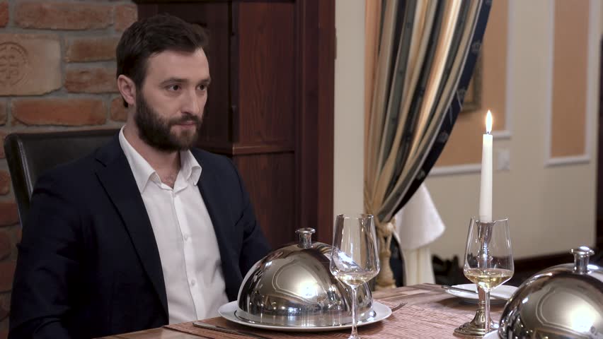 Two waiters simultaneously opens tableware cover - cloche showing the dish in front of the respectable bearded man in a suit. Fine dining restaurant concept. Royalty-Free Stock Footage #1011381923