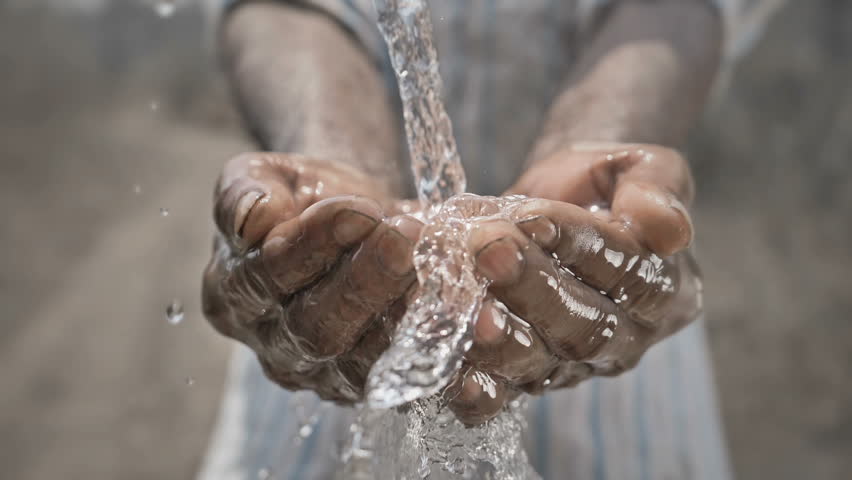 Slow motion shot of splash of freshwater falling on poor man's hands against barren and dry farmland. Clean drinking water splashing on hands of the poor rural man in a drought affected area  | Shutterstock HD Video #1011383468