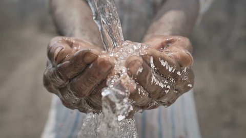 slow motion shot of splash of freshwater falling on poor man's hands against barren and dry farmland. Clean drinking water splashing on hands of the poor rural man in a drought affected area 
