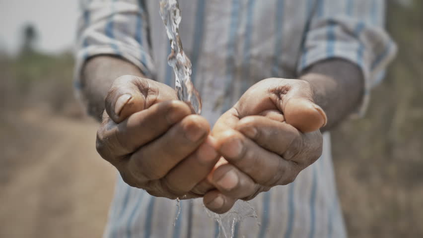 Real time shot of splash of freshwater falling on poor man's hands against barren and dry farmland. Clean drinking water splashing on hands of the poor rural man in a drought affected area Royalty-Free Stock Footage #1011383471