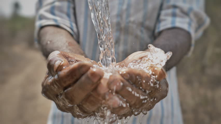 Real time shot of splash of freshwater falling on poor man's hands against barren and dry farmland. Clean drinking water splashing on hands of the poor rural man in a drought affected area | Shutterstock HD Video #1011383471
