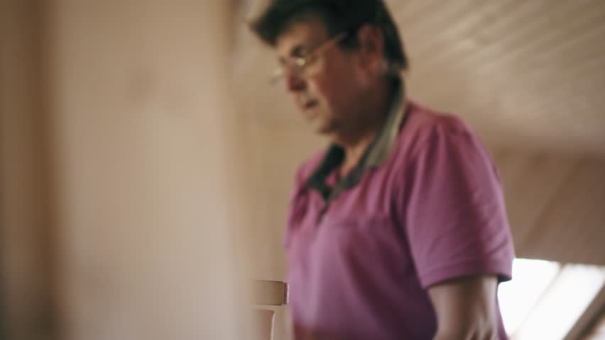 Construction worker puts a bucket with solution of cement on the stand with an effort. Hardworking job of a repair man
