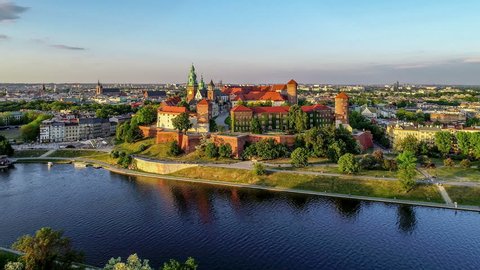Royal Wawel Cathedral and castle in Krakow, Poland, with Vistula river, park, yard and tourists. Aerial 4K approach video at sunset in spring. Old city with St. Mary church in the background