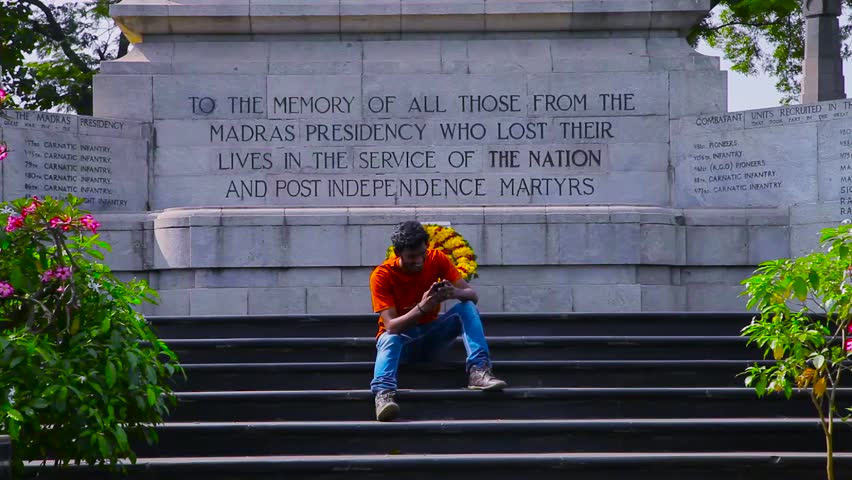 Happy smiling young man sitting and text message on smart phone, war memorial background.