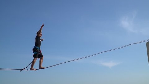 A man walks a tight rope and approaches the edge of a skyscraper