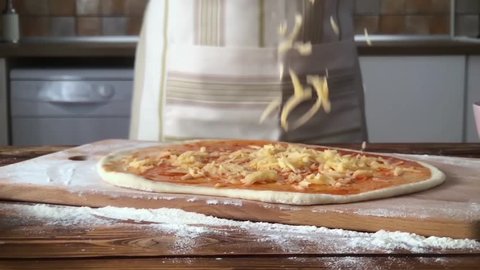 A female hand sprinkles a pizza with grated cheese close-up. super slow motion