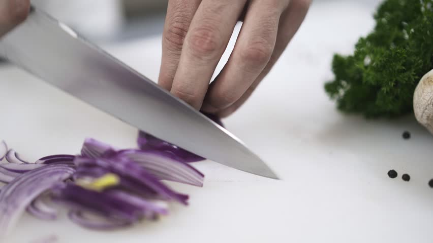 Unrecognizable chef chopping purple onion on a restaurant kitchen. Concept of high quality food. Locked down real time close up shot