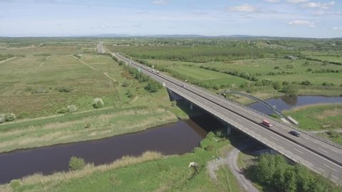 aerial birds eye view of a busy irish motorway with bridge crossing a water river and railway track in ennis county clare, ireland
