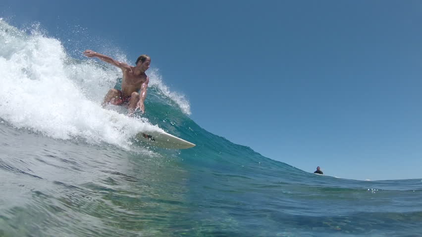SLOW MOTION, UNDERWATER: Fit extreme sportsman rides a small breaking wave while his friend watches him. Pro surfboarder catches a crystal clear wave while riding Cloudbreak waves in beautiful Fiji. | Shutterstock HD Video #1011441068