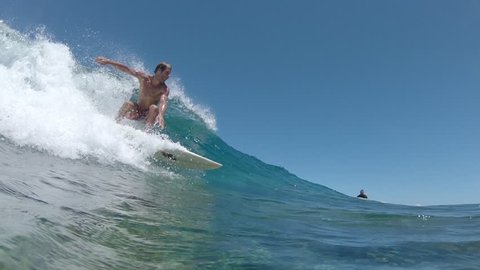 SLOW MOTION, UNDERWATER: Fit extreme sportsman rides a small breaking wave while his friend watches him. Pro surfboarder catches a crystal clear wave while riding Cloudbreak waves in beautiful Fiji.