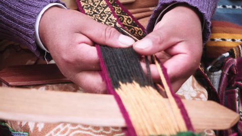 Indigenous woman selects the yarn meanwhile weaves yarn a foot loom at downtown Cusco, Peru.