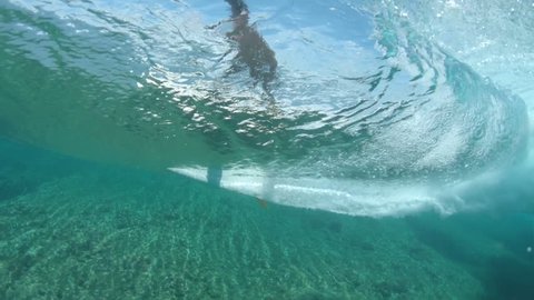 SLOW MOTION, LOW ANGLE, UNDERWATER: Athletic surfer girl rides an awesome crystal clear ocean wave in sunny Fiji. Fit Caucasian female tourist surfing a beautiful barrel wave on a perfect summer day.