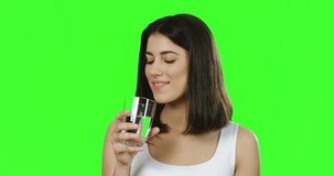Close up of the beautiful young woman in the white T-shirt drinking water from the glass in front of the camera on the green background. Chroma key.