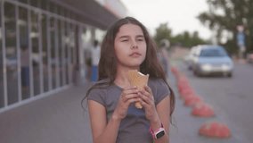 little girl eating ice cream goes down the street in the city next to the supermarket with a soft toy motion slow motion video. girl and ice cream urban eat lifestyle concept