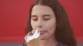 Pretty baby girl kid eating slow motion video nursing bottle licking big ice cream in lifestyle waffle cone with raspberry happy laughing on red background. the girl teenager and ice cream concept