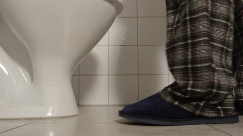 Closeup of male legs in a pajamas and slippers comes to a toilet