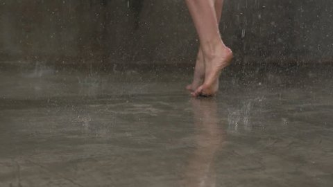 Close-up foots of ballerina who is dancing ballet elements of movement during tha water rain in indoors slow motion. Dancer dancing in the rain, slow motion