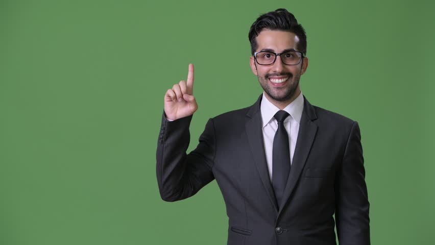 Young handsome bearded Persian businessman against green background