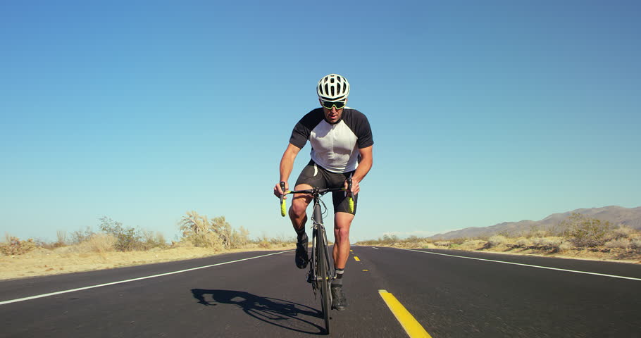 Slow motion young healthy man cycling on road bike outside on desert road on sunny day with blue sky in background | Shutterstock HD Video #1011457715