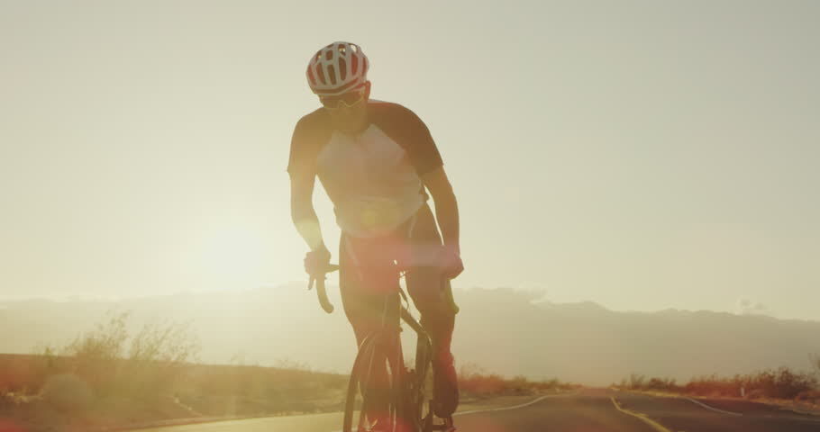 Slow motion young man cycling on road bike outside on desert road at sunset with lens flare | Shutterstock HD Video #1011457787