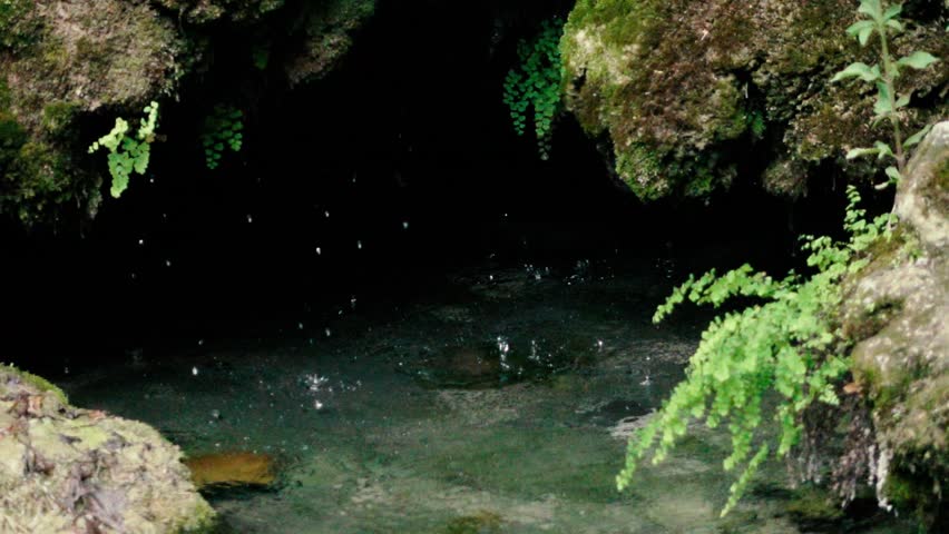 Slow motion footage. Drops drip into the water in a small cave