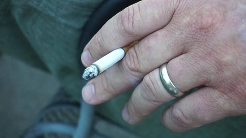 person holding cigarette as it burns and smokes.  one male hand holds his tobacco. 
