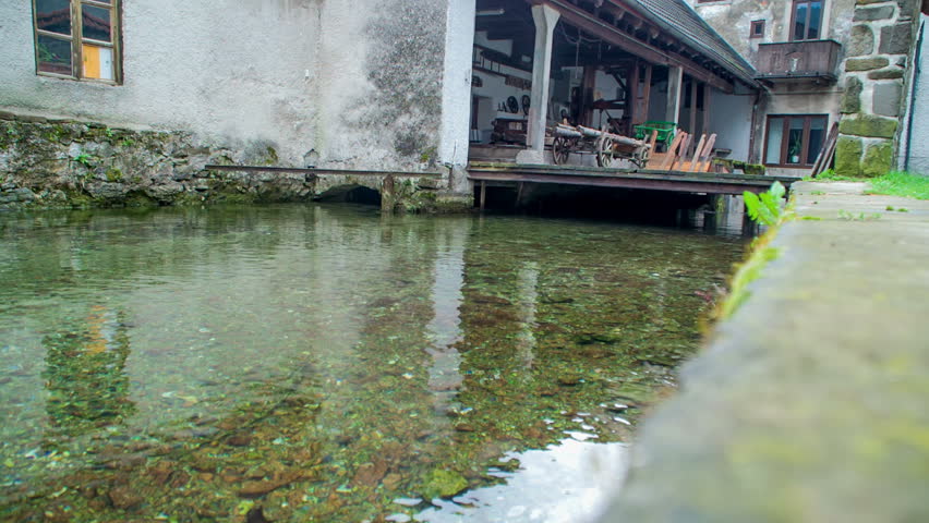 There are lots of small stones seen in the river. The river flows under the surface of a big house in the Slovenian Karst.