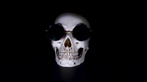 Skull in round sunglasses on a black background. close-up. 4k, dolly shot, defocusing, blur.