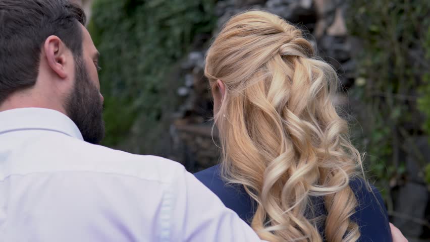 Man is walking with his couple down the street in windy weather. His jacket is on the shoulders of a woman. View from the back.
