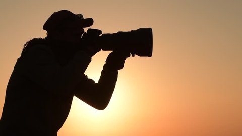 Safari Outdoor Photographer at Sunset. Silhouette of Men Keeping Digital Camera in Hand with Large Telephoto Lens For the Better Wildlife Closeups. Slow Motion Footage
