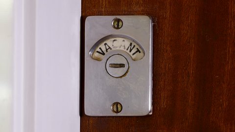 Closeup of someone entering a public toilet / bathroom and closing the wooden door. The sign changes from vacant to engaged.