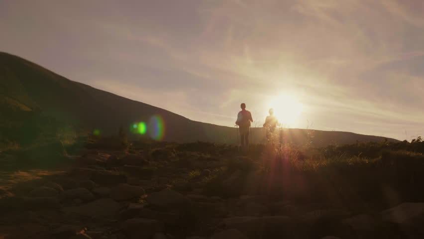 Romance of an active way of life. A couple of tourists in the rays of the setting sun go along the mountain trail