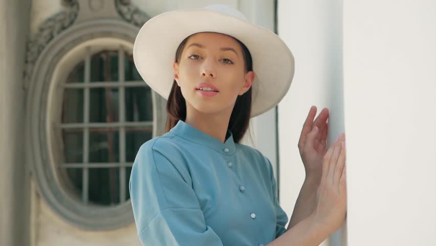 Portrait of Happy Stylish Charming young mixed race woman Fashion Blogger in blue summer dress and white hat posing on the summer street, sun is shining