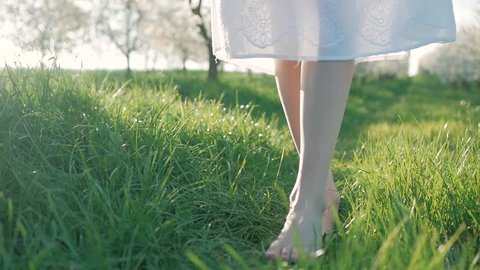 Slow motion shot of bare feet of young girl walking and running on green grass