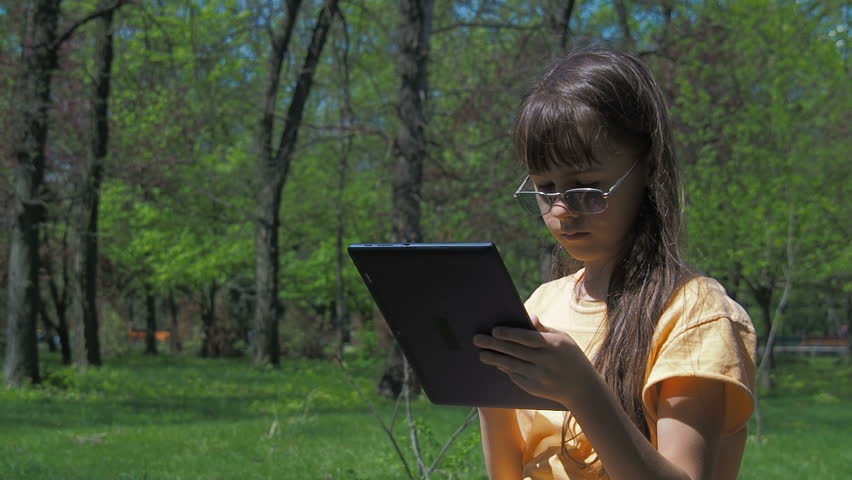 Child in nature with a gadget. Little girl with a tablet in the park.