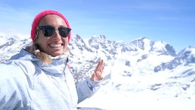 Cheerful young woman taking a selfie portrait photography by above the ski slopes with 360 view on top of snowcapped mountains in the Swiss Alps, Switzerland. 4K resolution video