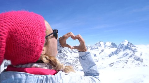 Young woman on ski slopes making heart shape on the stunning landscape. Woman on ski vacation in Switzerland, loving nature. 4K resolution 