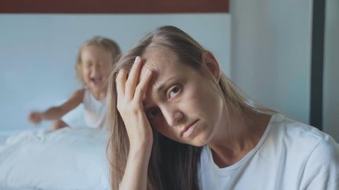Portrait of upset tired mother with angry little child girl screaming and beating pillow on the background. A hyperactive difficult kids and despairing parents concept.