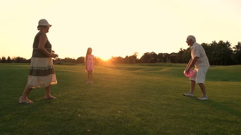 Active family rest on nature with ball. Slow motion senior people and their granddaughter having fun with ball in countryside, sunset sky. Active elderly people.