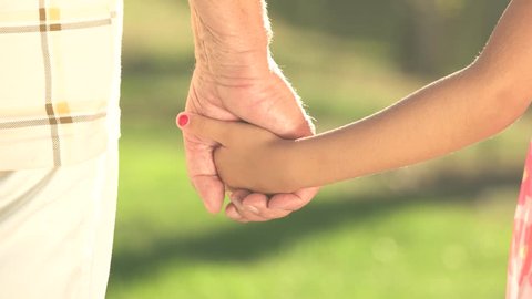 Old man and kid holding hands together. Grandpa and granddaughter detached hands holding together, summer nature background.