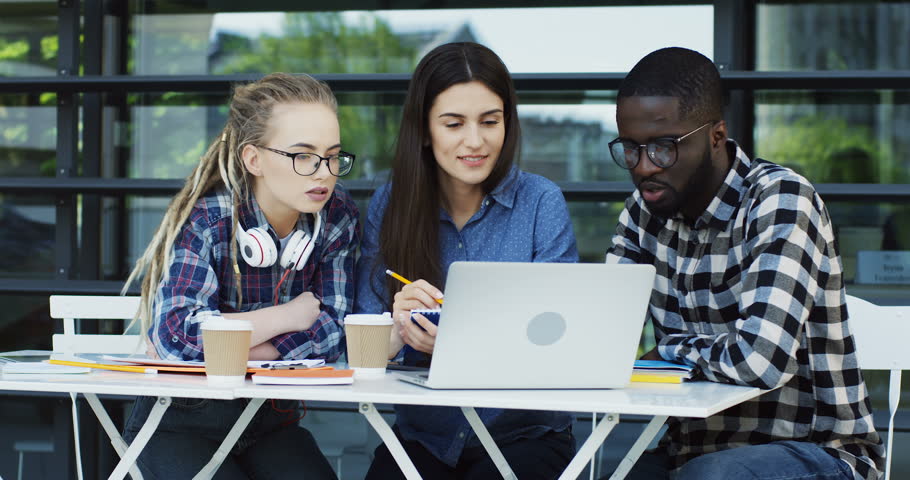 Multhiethnic students having a break between their classes, resting with a coffee and discussing studing project on a laptop computer. Outdoors