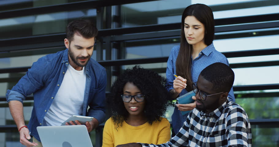 Group of multiethnic students planning their studing project and discussing it at the laptop computer outdoor.
