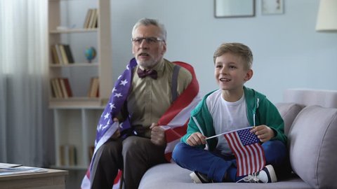 Boy and grandpa waving American flag, watching sport game at home, happy for win 库存视频
