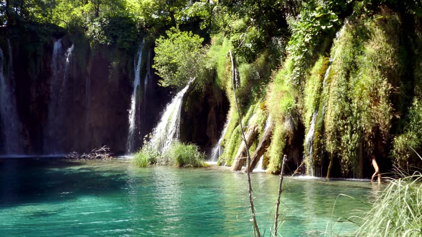 Right to left pan of waterfalls falling in the crystal clear blue lake in Plitvice Lakes National Park